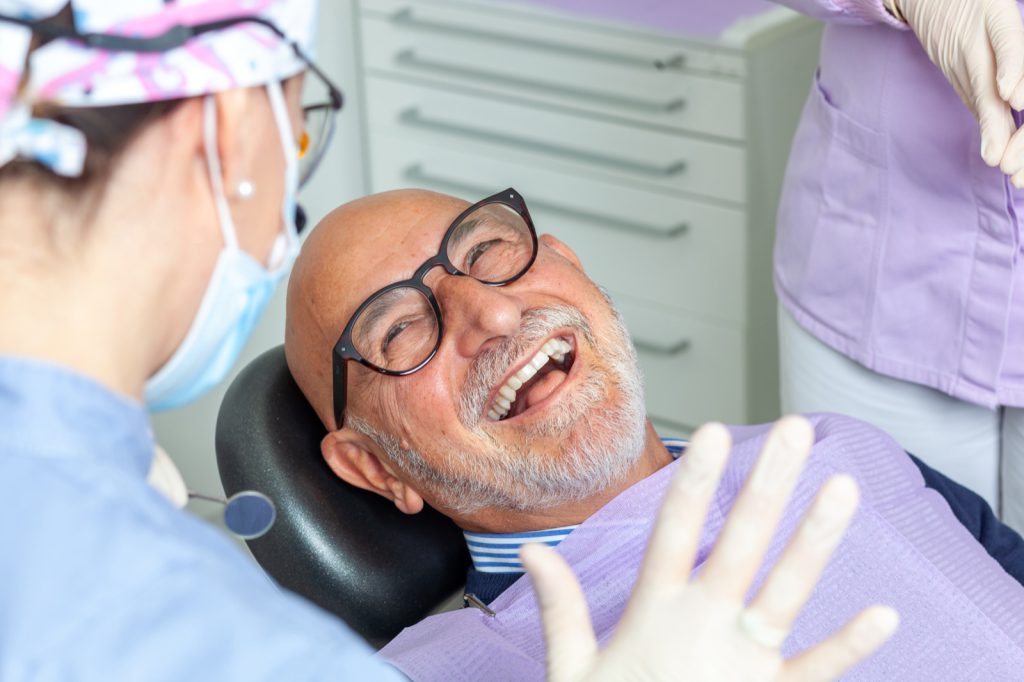 Happy senior man engaging in conversation and sharing laughter with a female dentist during a dental checkup at the clinic